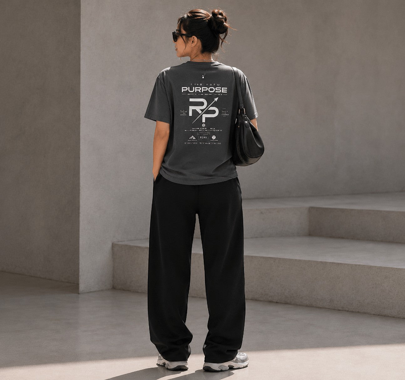 Rise With Purpose dark grey Sorona t-shirt with graphic print on back, worn by a woman with loose black pants.