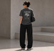 Rise With Purpose dark grey Sorona t-shirt with graphic print on back, worn by a woman with loose black pants.