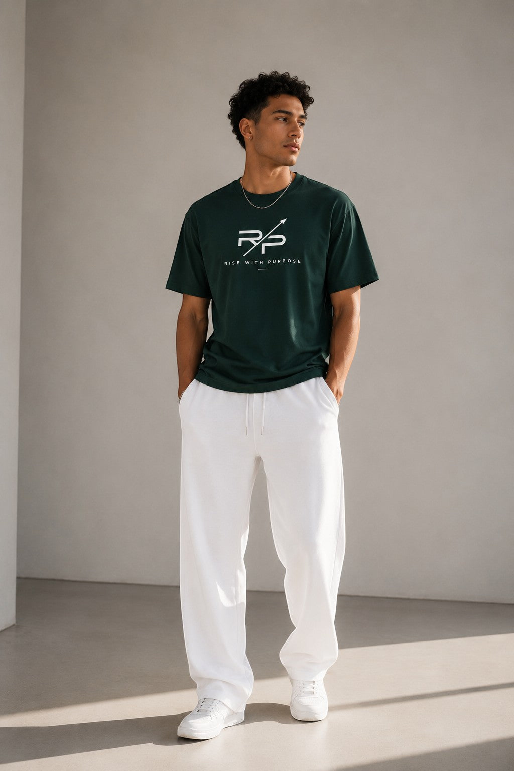 Rise With Purpose dark green Sorona t-shirt with white logo print, worn by a man with white pants.